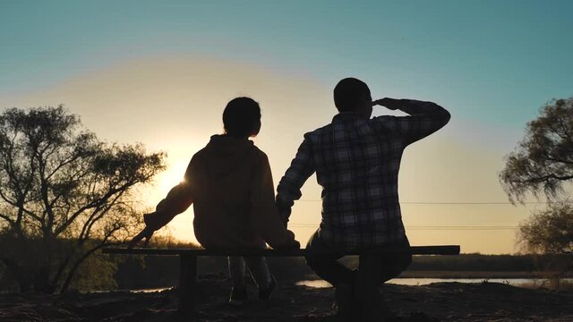 happy family man and girl teamwork sitting on a bench silhouette sunset in the park and nature. dad and daughter lifestyle relax in the park spend together. couple in love hold hand sit back look at