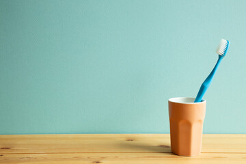 Blue toothbrush in cup on wooden table with mint background. copy space