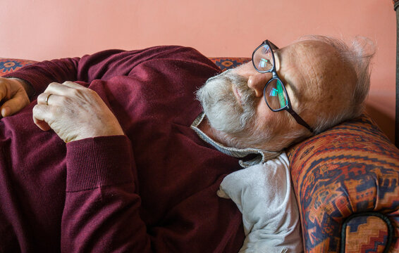 Bearded old man sleeping on sofa at home. Elderly man felt asleep on sofa. Ill grandfather having rest at living room. Health care / Healthcare concept.