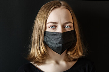 Young girl in a black protective three-layer facial surgical mask. The concept of life in the coronavirus pandemic and after. The new is normal in the Covid-19 epidemic.