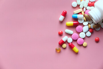 Top view of colorful pills spilling from container on pink 