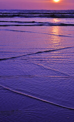 Sunset is taken at the ocean (Long Beach Washington) with interesting patterns of the waves coming in to shore on the sand in the vertical image of natural beauty.  