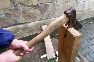 Close-up of axe ready for cutting logs in mans hands. Cutting wood in the yard concept. Already chopped firewood laying in the background. work of a lumberjack and a villager