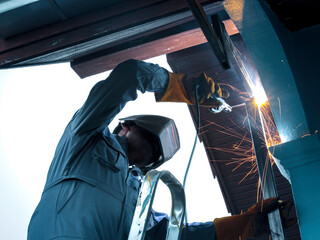 Industrial worker wearing safety mask, helmet, and safe glasses welding metal construction on...