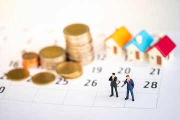 Miniature people: Two business man on calendar stack of coin and home with copy space for text using as background saving, investment, money, financial, business analytics concept.