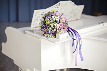 Purple Bridal bouquet decorated with ribbons lies on the white piano