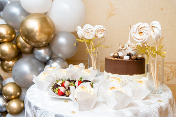 Festive table with sweet cakes and fruit in chocolate, beautiful umbrellas in the background.