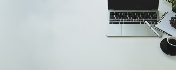 Copy space working desk that surrounded by computer laptop, pen, note, coffee cup, potted plant and pine cone.