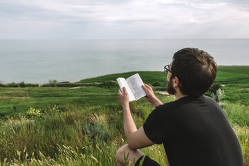 Man is reading a book on a mountain seashore alone, outdoor recreation.