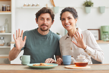 Fototapeta na wymiar Portrait of young happy couple having breakfast and smiling at camera while sitting at the table in the kitchen