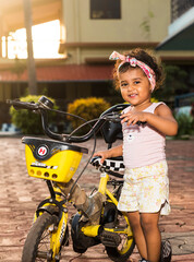 Obraz premium Playful Pretty Indian girl child/infant/toddler wearing a hair band, playing with a cycle/tricycle. Kid giving joyful expressions