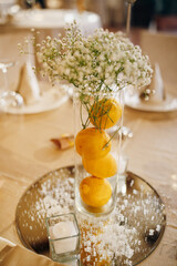 Composition with lemons and flowers in transparent vase on banquet table