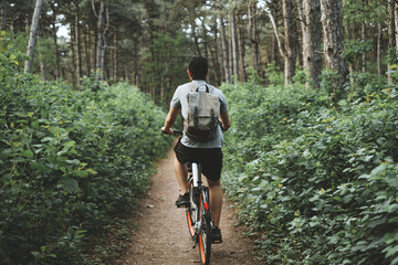 Young man with backpack cycling on a forest path, active lifestyle, playing sports in nature.