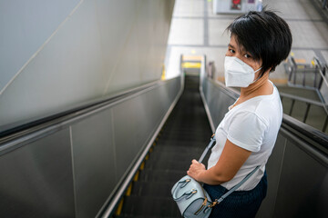 Fototapeta na wymiar Asian woman wearing face mask and keep distance to other people while using escalator in subway station during coronavirus or covid-19 outbreak. social distancing, quarantine or new normal concept