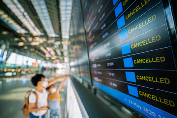 Asian female traveler looking on  flights information board in airport and it show flights cancellation status on because coronavirus or covid-19 pandemic effected. airline business crisis concept