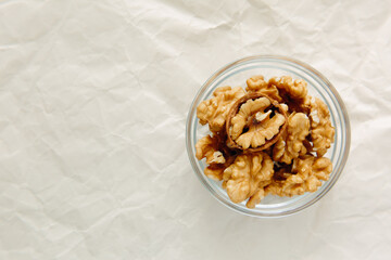 Peeled walnuts in round bowl, close-up, on light background. View from above.