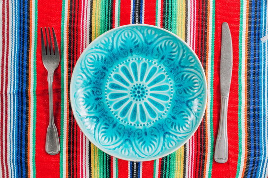 Festive Mexican table setting. Plate and cutlery with colorful napkin on rustic wooden background. Flat lay.