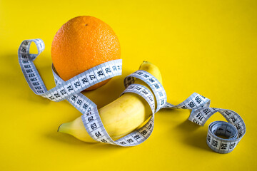 Orange and banana with tape measure on yellow background. Healthy lifestyle concept