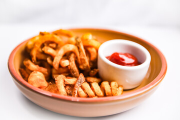 Curly fries on brown plate with white background side of ketchup close up