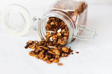 A jar of home made granola spilling on to a white table top. This granola is made from roasted oats...