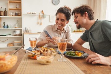 Young smiling woman showing some pictures on her mobile phone to her boyfriend during dinner in the...