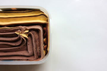 Orange and chocolate ice cream in a plastic box on white background with copy space. Selective focus
