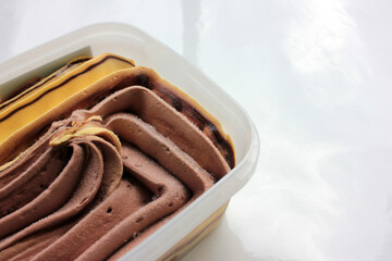 Orange and chocolate ice cream in a plastic box on white background with copy space. Selective focus

