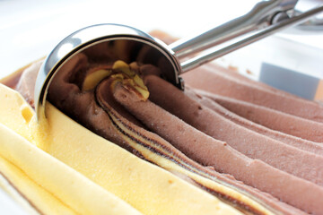 Scoop ice creame process. Textured orange and chocolate ice cream in a plastic box on white background with copy space. Selective focus
