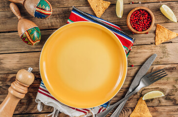Festive Mexican table setting. Plate and cutlery with colorful napkin on rustic wooden background....