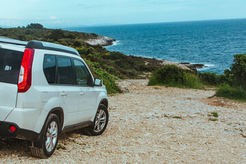 Fototapeta na wymiar white suv car at rocky beach near sea. car travel concept