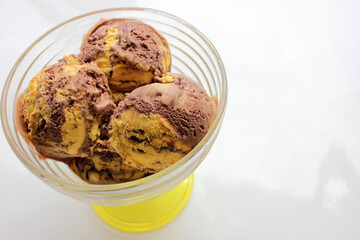 Scoops of orange and chocolate ice cream in a glass dessert bowl on white background with copy space. Selective focus

