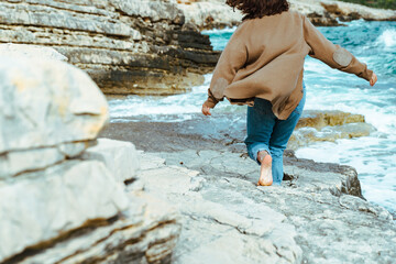woman walking by rocky sea beach at sunny windy day. summer vacation