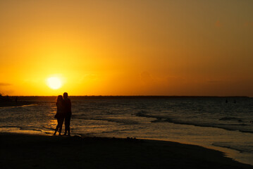 Fototapeta na wymiar Couple hugging each other in front of a golden sunset on the beach