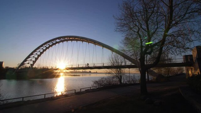 Bicyclist rides through sun on Mimico bridge at sunrise. Toronto.