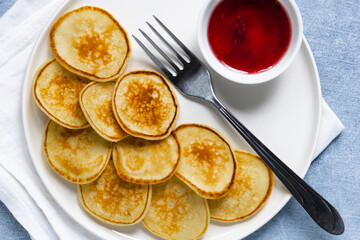 Trendy pancake cereal meal. Tiny baked pancakes with berry jam on white plate.. Breakfast food at home.