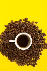 Black coffee in the white cup and coffee beans  on the  yellow background. Copy space. Top view. Location vertical.