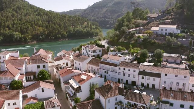 Flight over the mountain village of Dornes in Portugal. Drone footage of a picturesque village on a peninsula among a mountain river and green mountains.