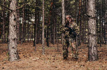 Forest sniper hunter in camouflage leaf and grass suit standing with rifle.