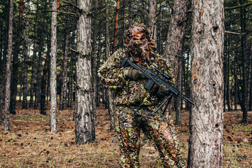 Forest sniper hunter in camouflage suit standing with rifle.