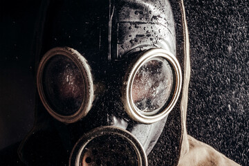 Stalker in wet soviet rubber gas mask on rain and black background.