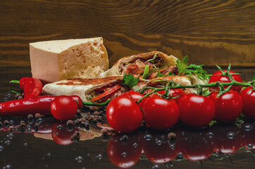 Composition of shawarma, red pepper, cherry tomatoes, cabbage, cheese on a black wood background