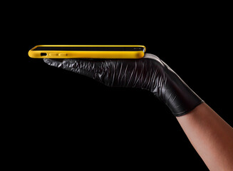 Hand in black glove holding mobile phone with blank screen isolated on black