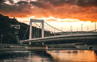 Elisabeth bridge over the Danube river in Budapest at sunset with the Gellert Hill in the background, dramatic sky with setting sun, Budapest cityscape, Hungary, suspension bridge