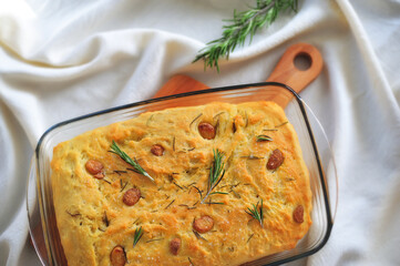 Focaccia with garlic and rosemary in a transparent baking dish on a wooden Board on a table covered with a white tablecloth