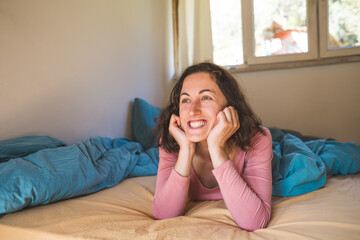 A smiling woman of thirty lies in bed after waking up.