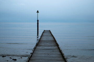 Naklejka premium Old wooden single pier leading into a foggy ocean with little variation from sky to water