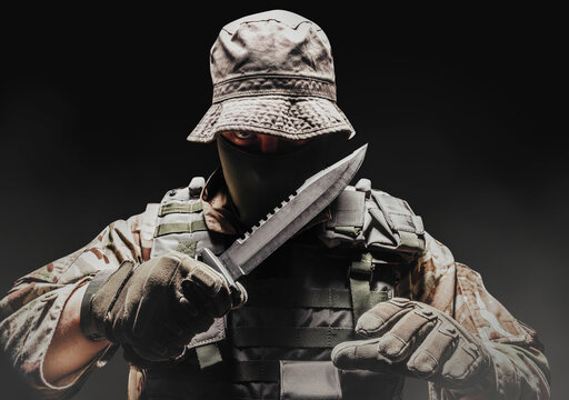 Fully equipped soldier in panama hat, armor vest and tactical gloves with knife on black background.