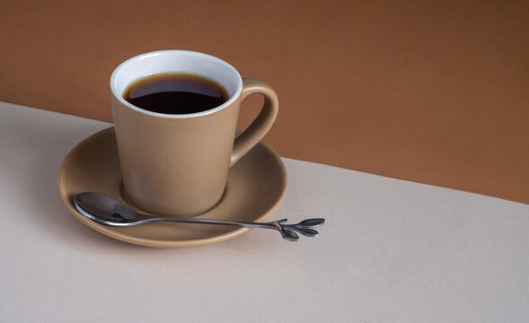 Сup of coffee on a beige and brown background.
Beige coffee pair with a decorative spoon. Monochrome colors. Copy space.