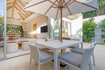 Exterior design in luxury pool villa feature pool terrace, garden landscape, outdoor dining table, BBQ, dining chair and umbrella overlooking to living room