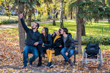 Young disabled woman in a wheelchair taking selfie with friends in a park